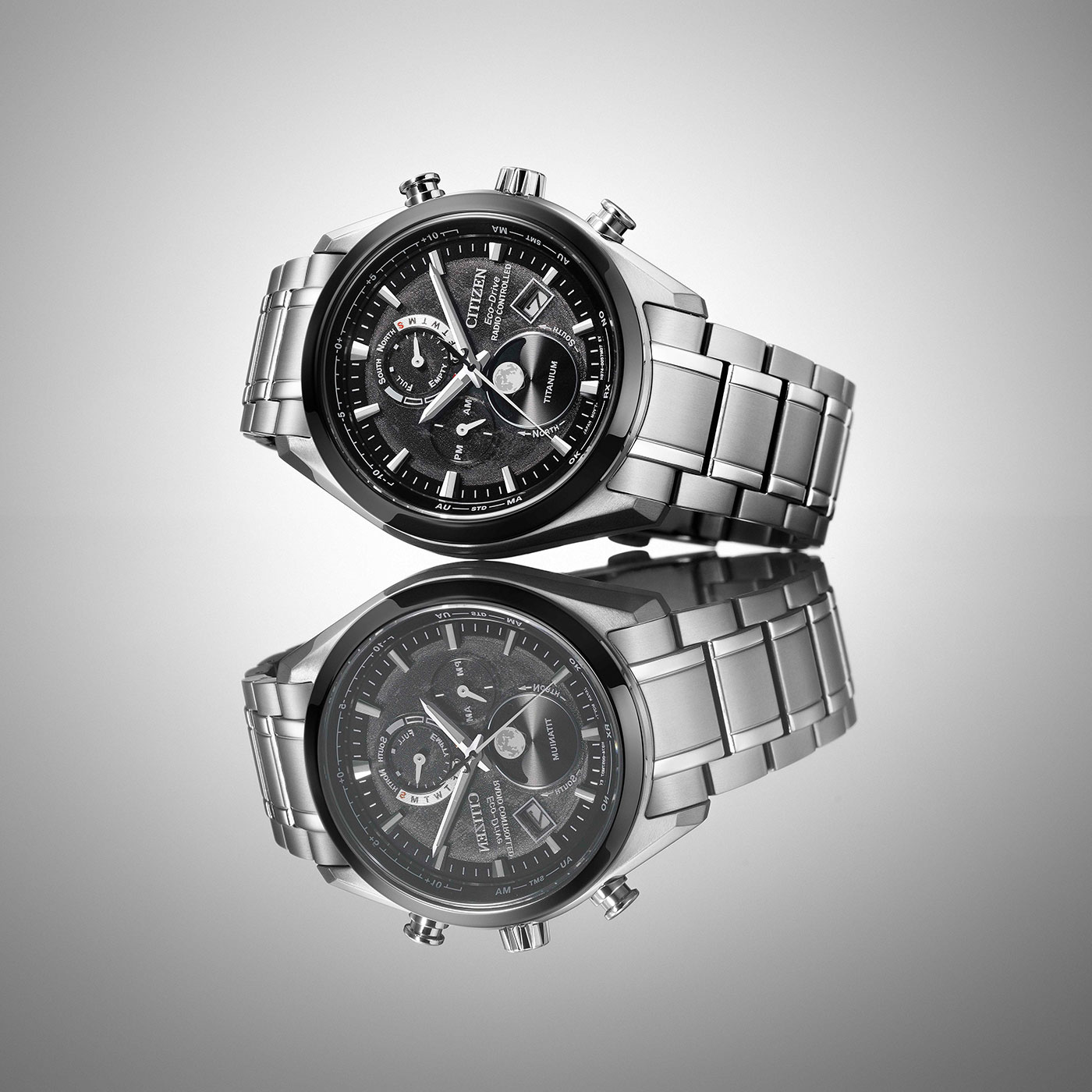 Citizen watch with a black face and silver band, reflected on a surface.
