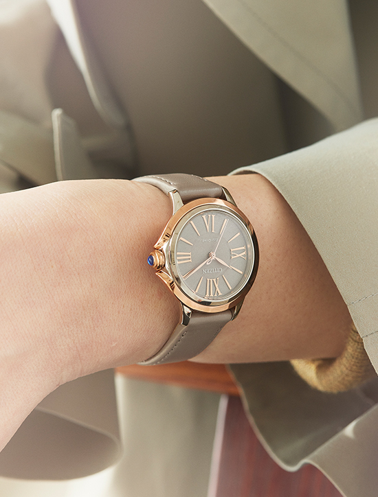 Close-up of a wristwatch on a wrist, with a grey strap and gold details.