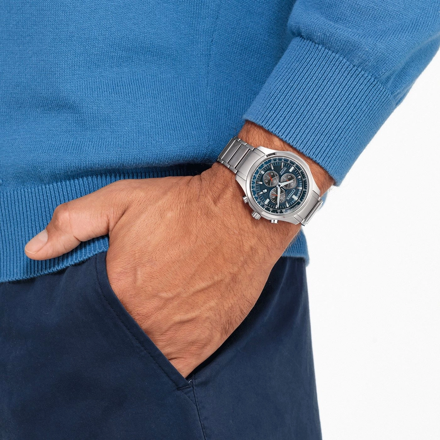 Man wearing a watch, blue sweater, and navy pants with his hand in his pocket.