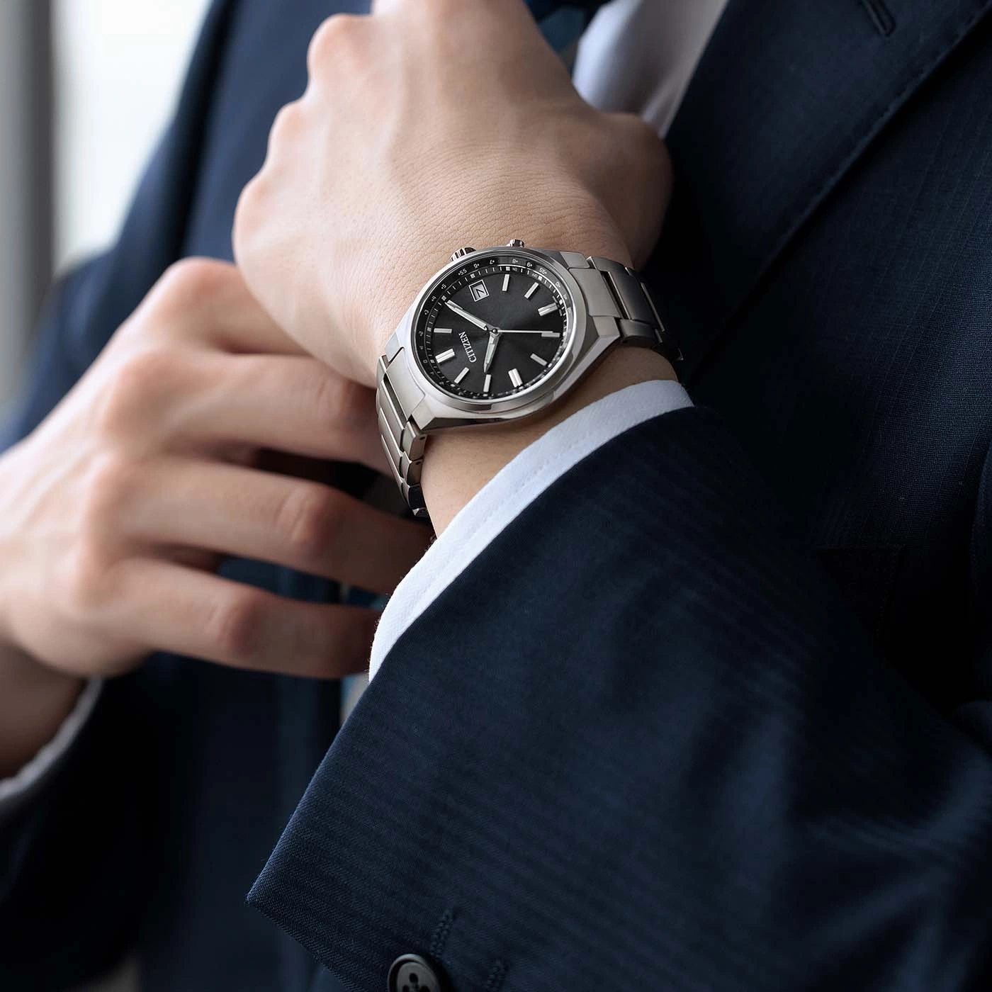 Man in a suit adjusting his tie, wearing a wristwatch.