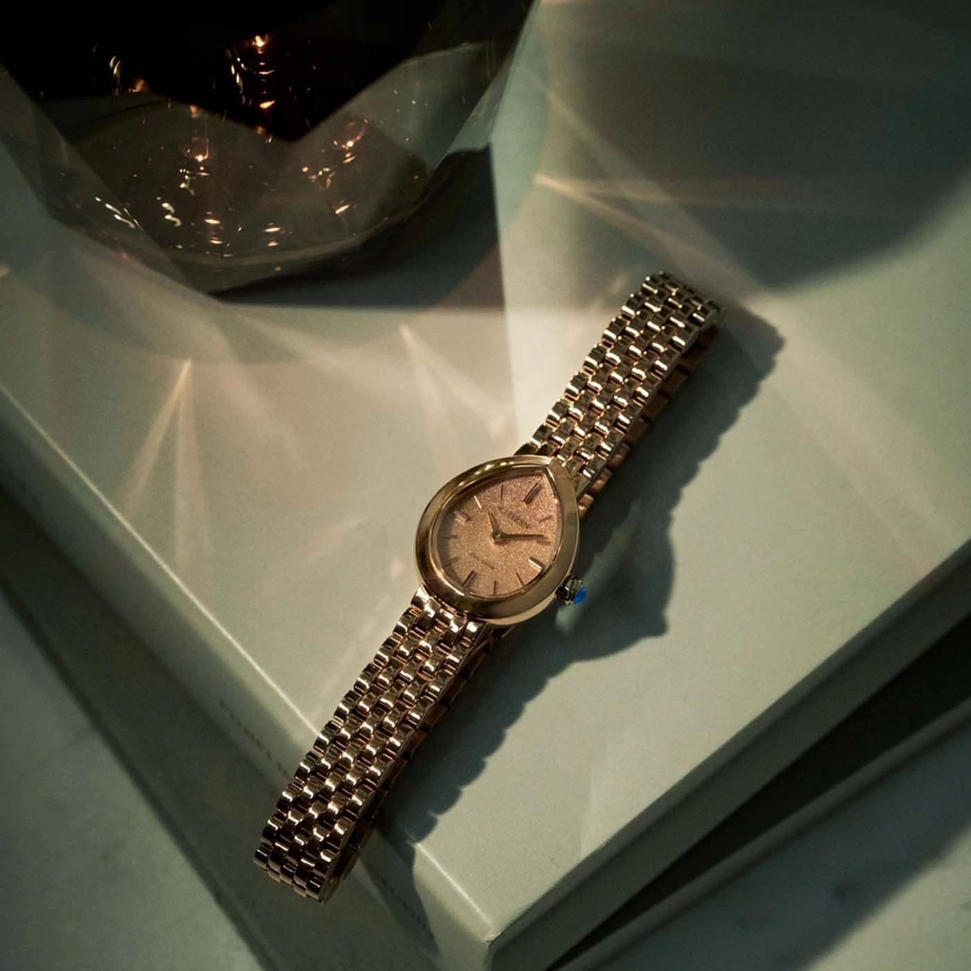 A gold watch with a patterned face rests on a light green surface.