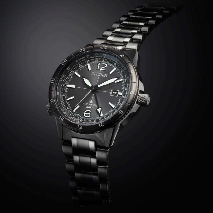 A stylish Citizen automatic GMT watch with a dark metal band, presented against a sleek, dark background.
