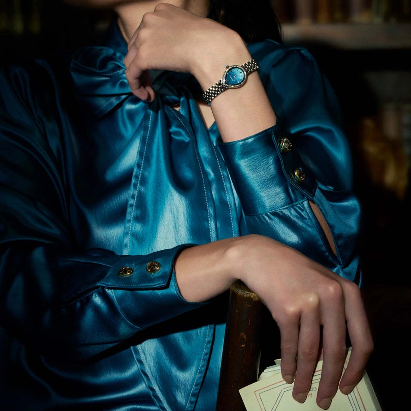 Woman in blue satin dress with watch and papers.