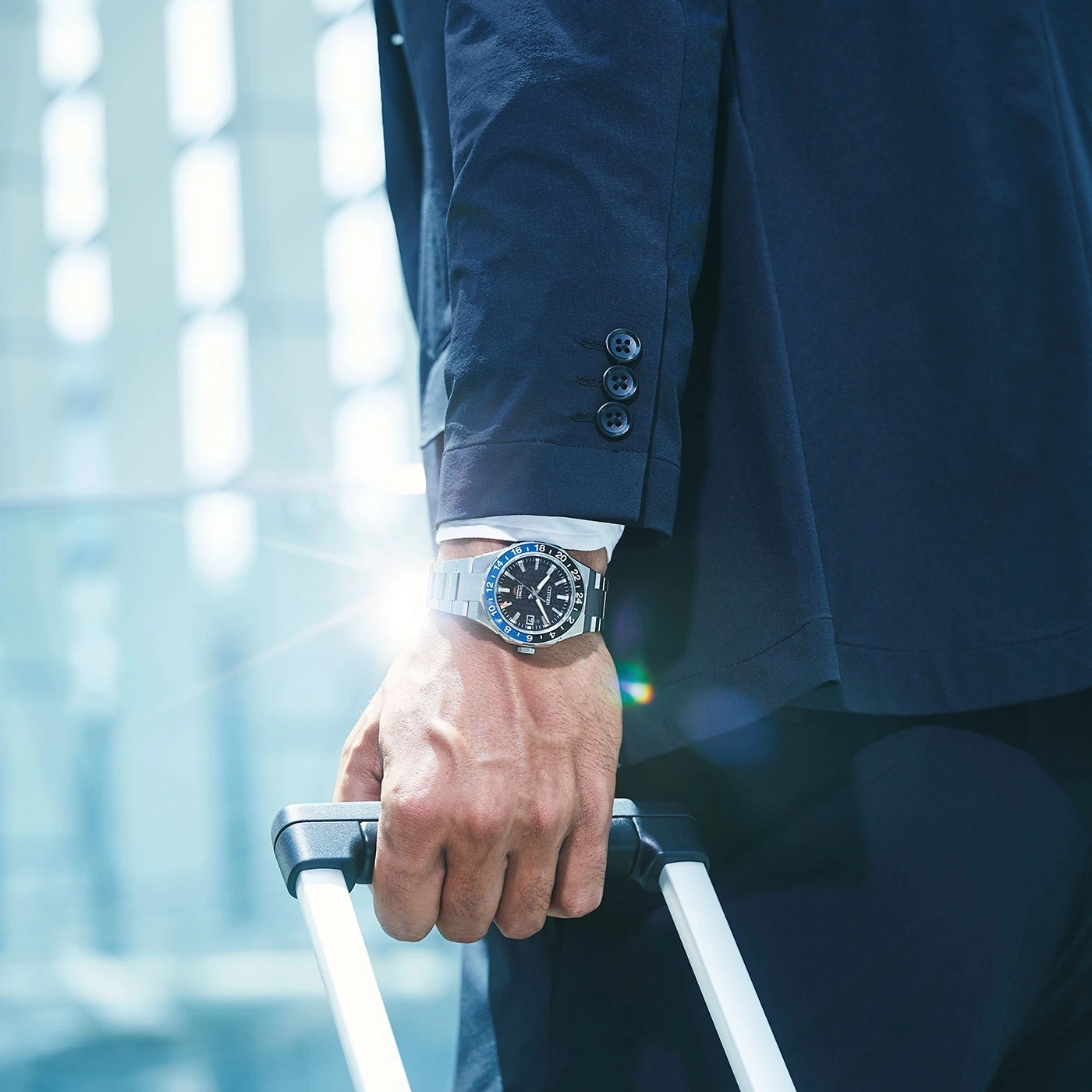Man in suit holding luggage, wearing a watch, business travel concept