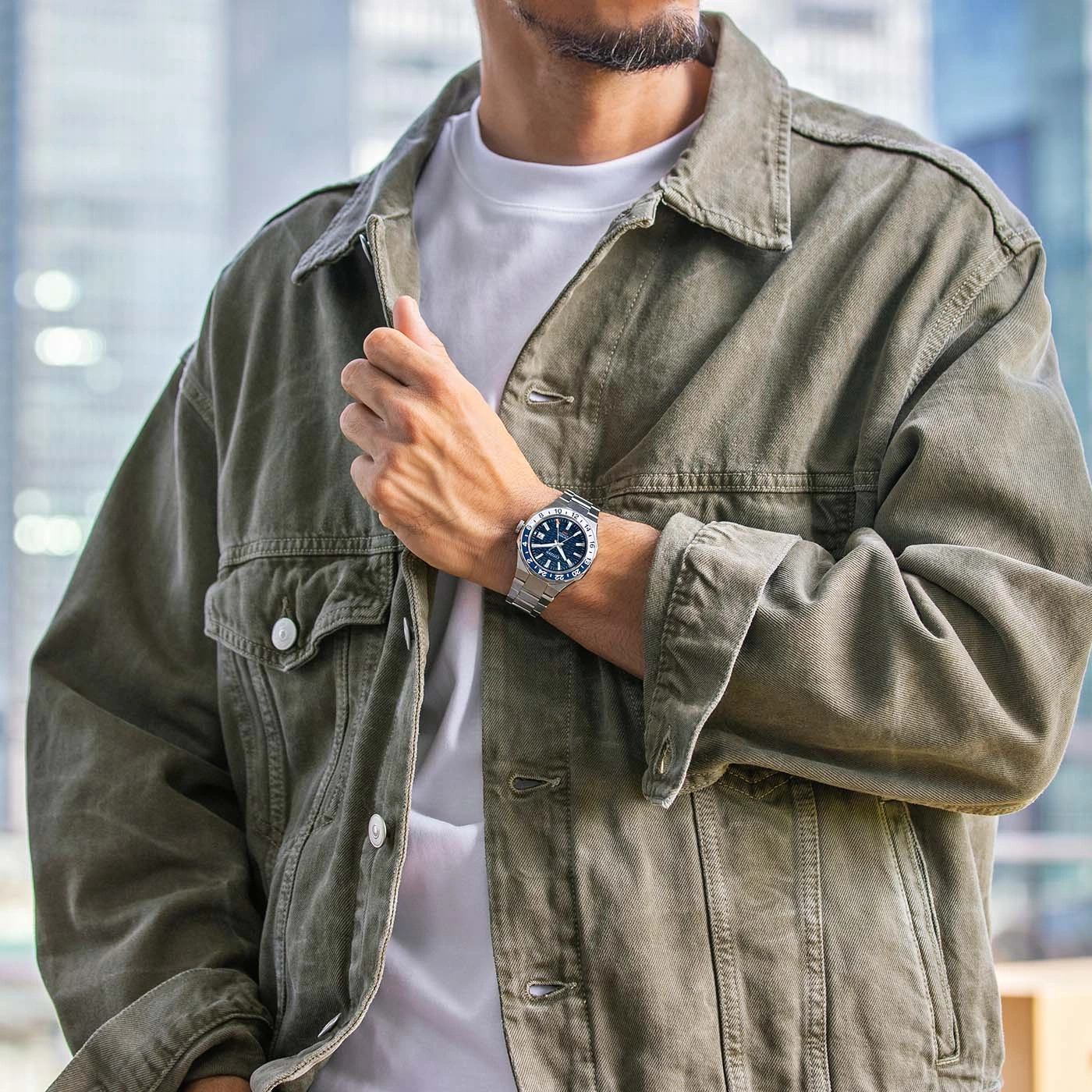 Man wearing a watch and a green jacket, posing for a photo.
