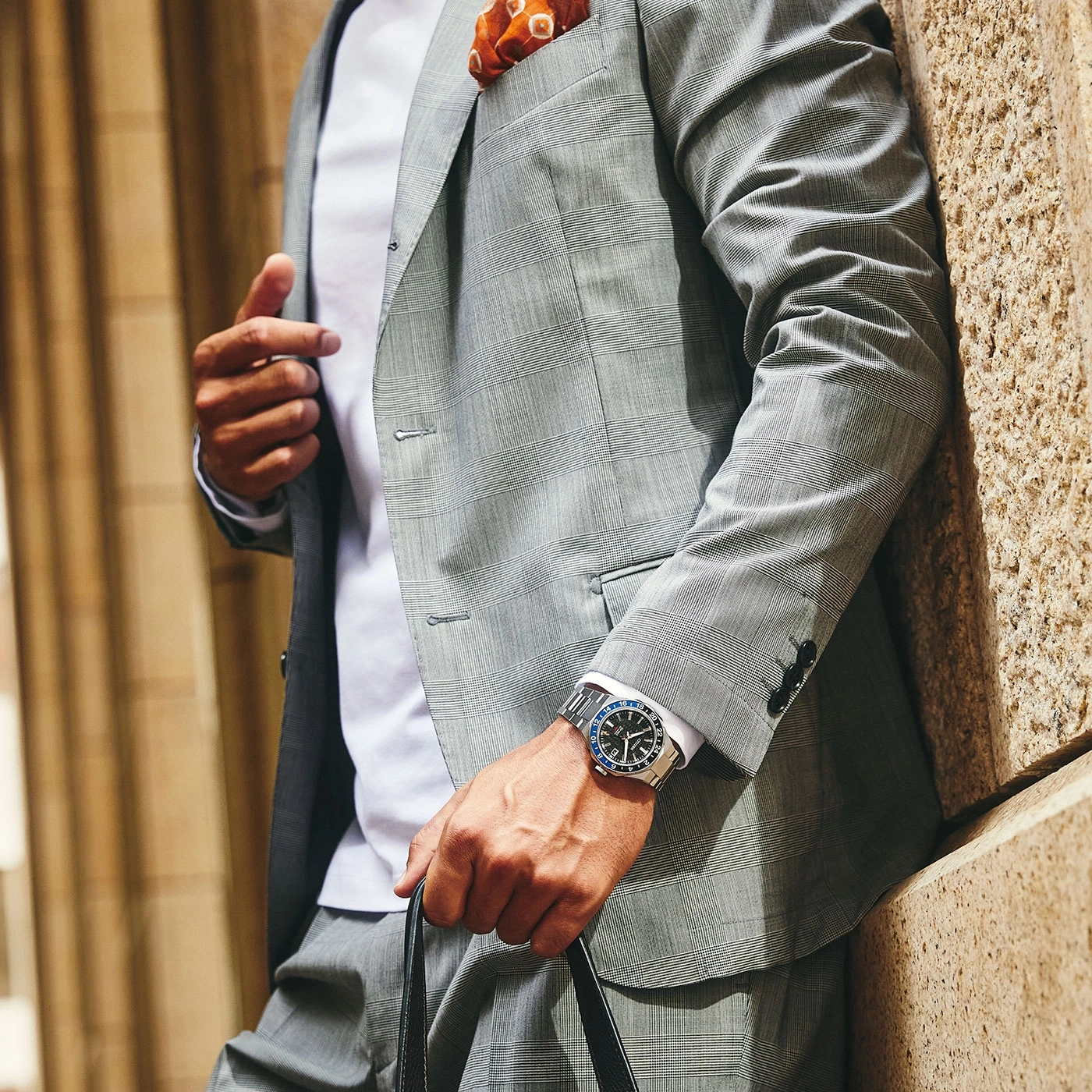 Man in suit with watch and pocket square leaning against a wall
