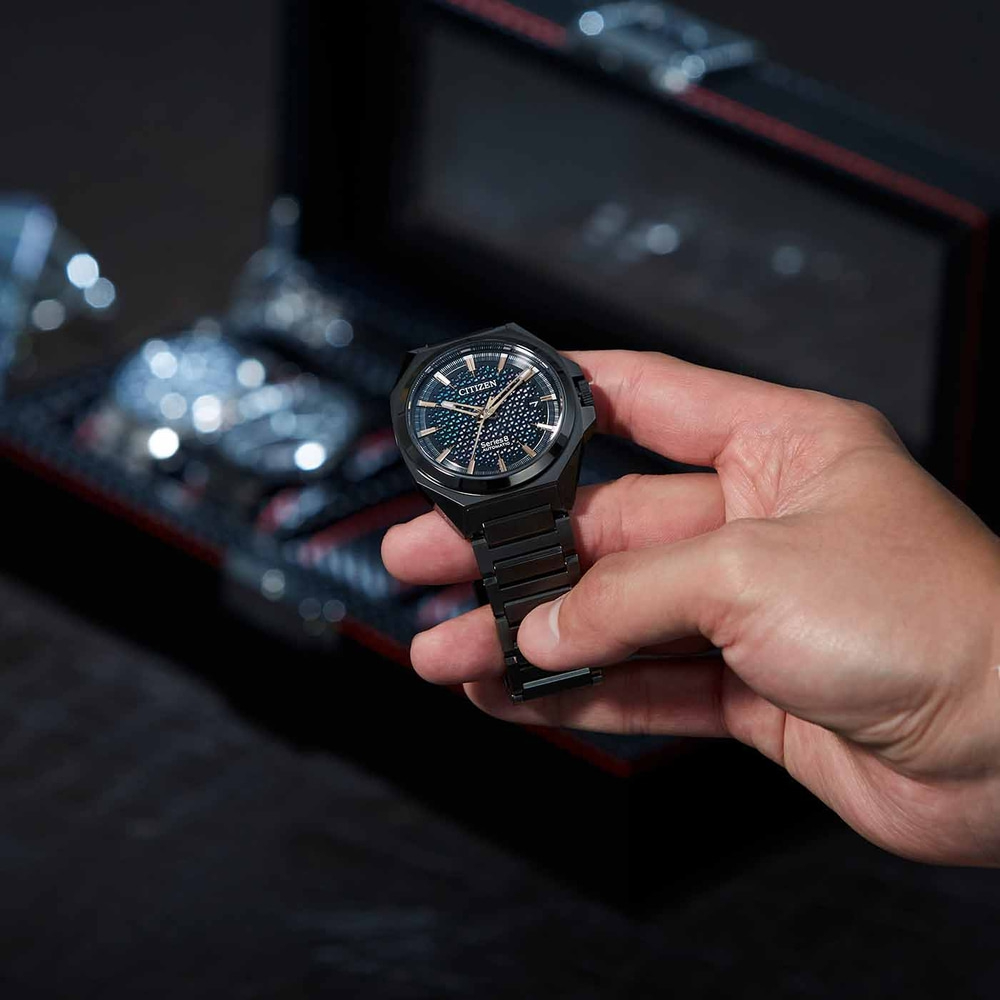 A person holding a black Citizen watch with a dark background.