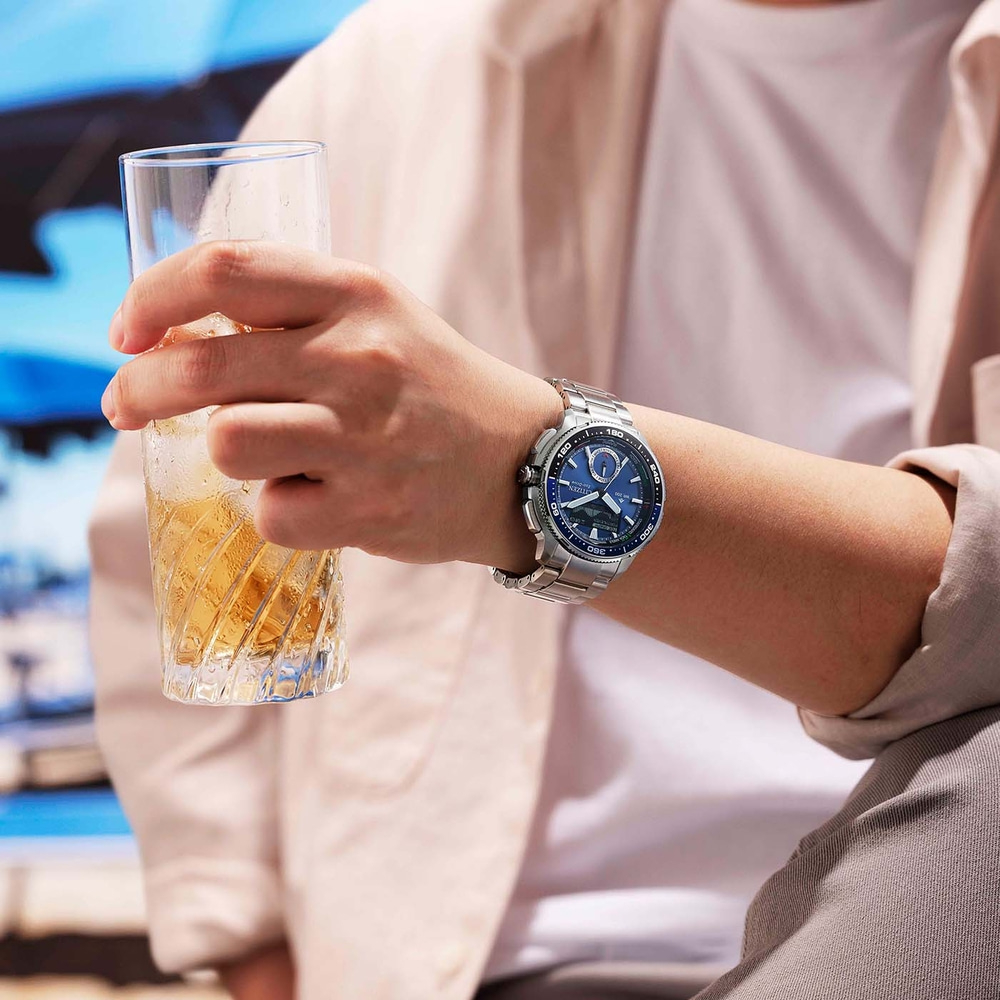 A person holds a glass of iced beverage and wears a silver watch.