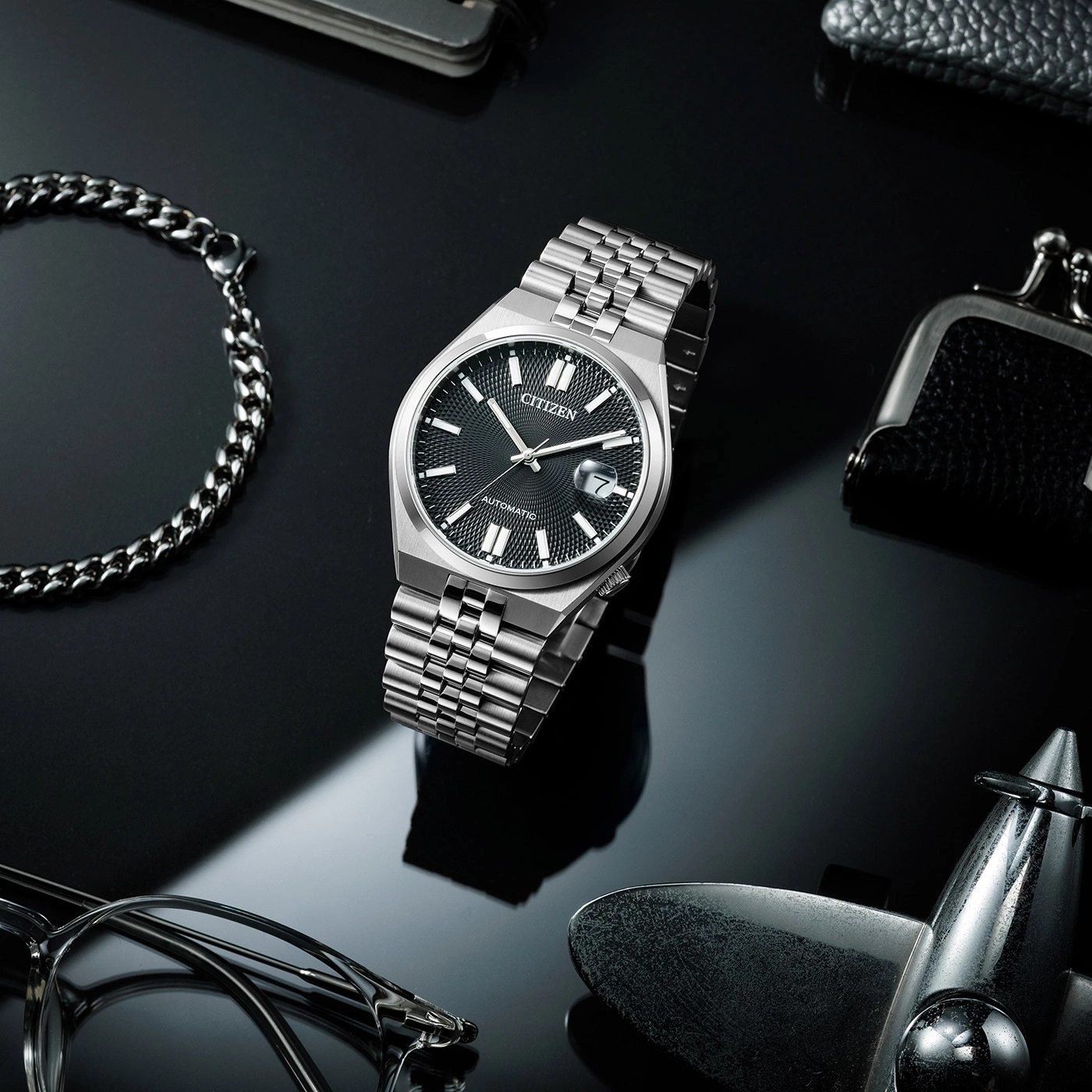 Citizen watch with bracelet, glasses, and accessories on a black surface.