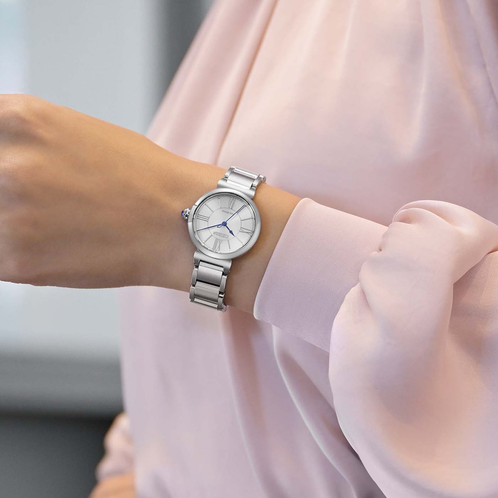 A woman's wrist wearing a silver watch with a white face and Roman numerals.