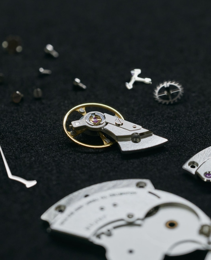 Close-up of watch parts on a black surface, intricate details visible.