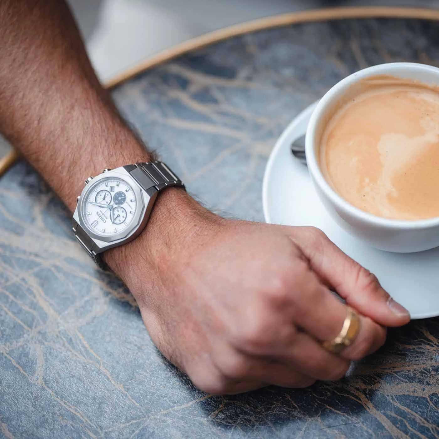 Man's wrist watch and coffee cup on a table, close-up shot.