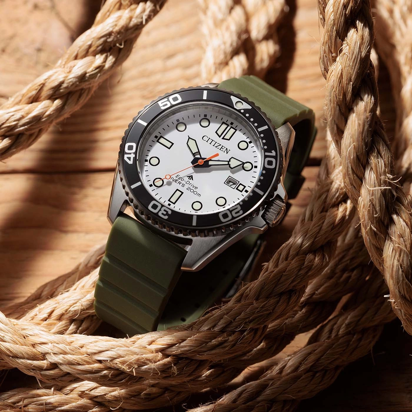 A Citizen Eco-Drive dive watch with a white face and green strap, resting on a wooden surface with rope.