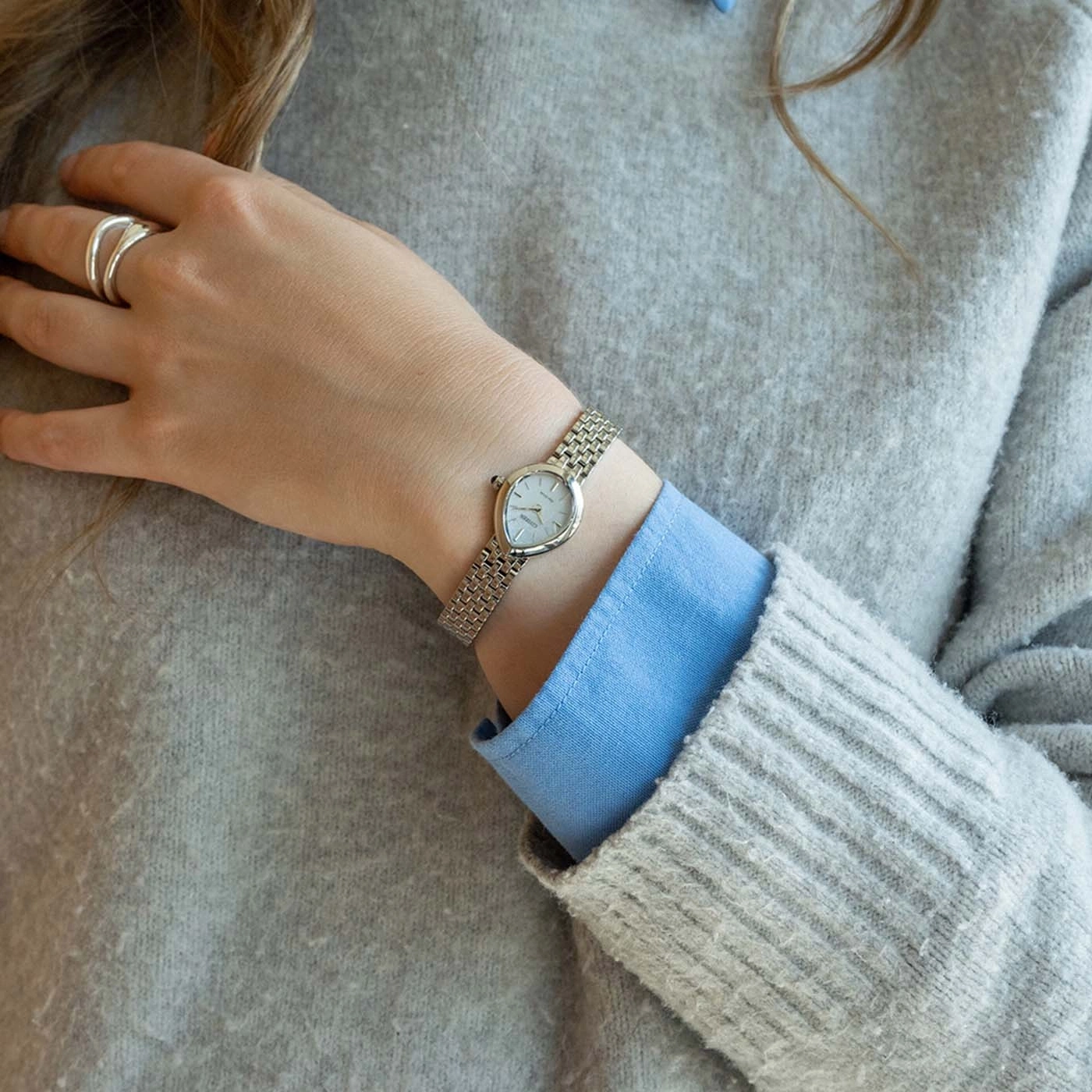 Woman wearing a sweater, shirt, watch, and ring.