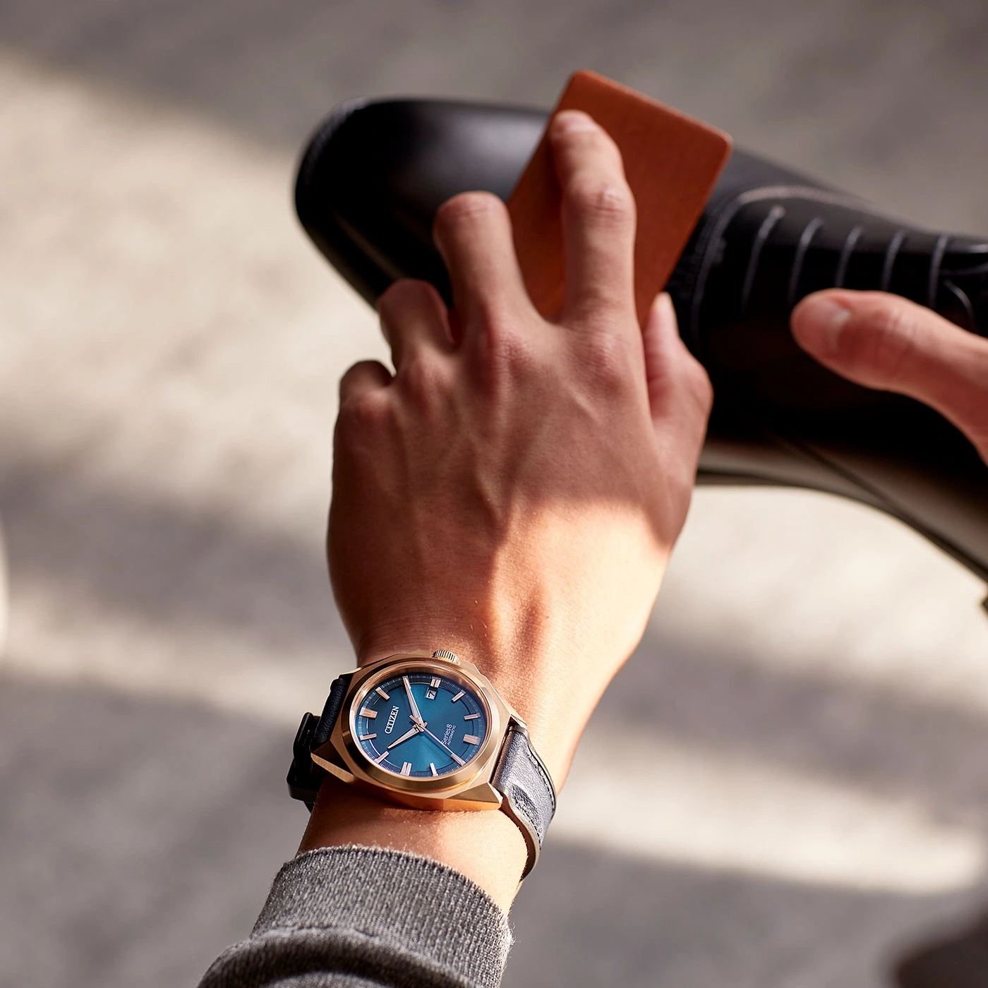 Man polishing a black shoe while wearing a gold watch with a blue face.