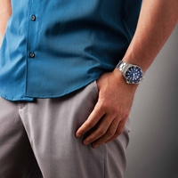 Man wearing a blue shirt and grey pants with a watch on his wrist.