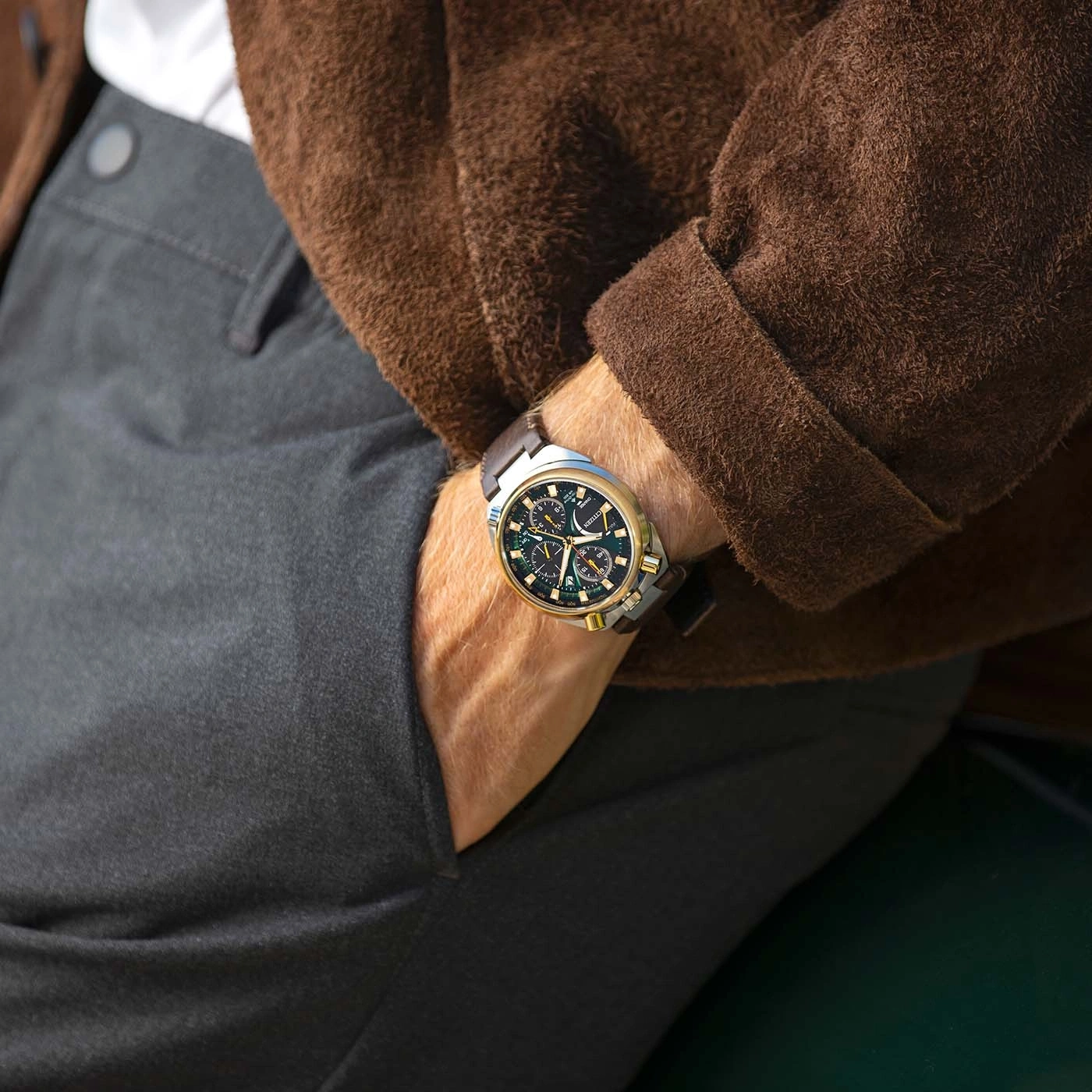 Man wearing a brown jacket, grey pants, and a watch.