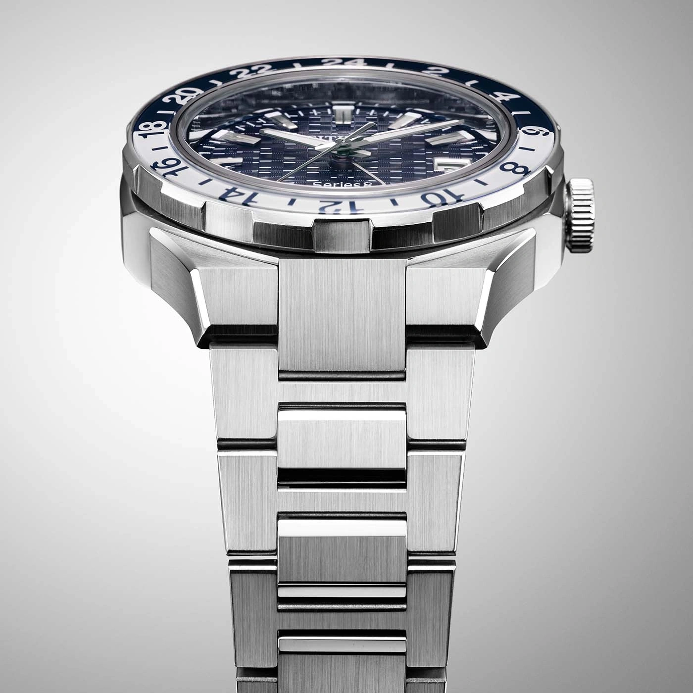 Close-up of a silver watch with a blue and white bezel and a metal strap.