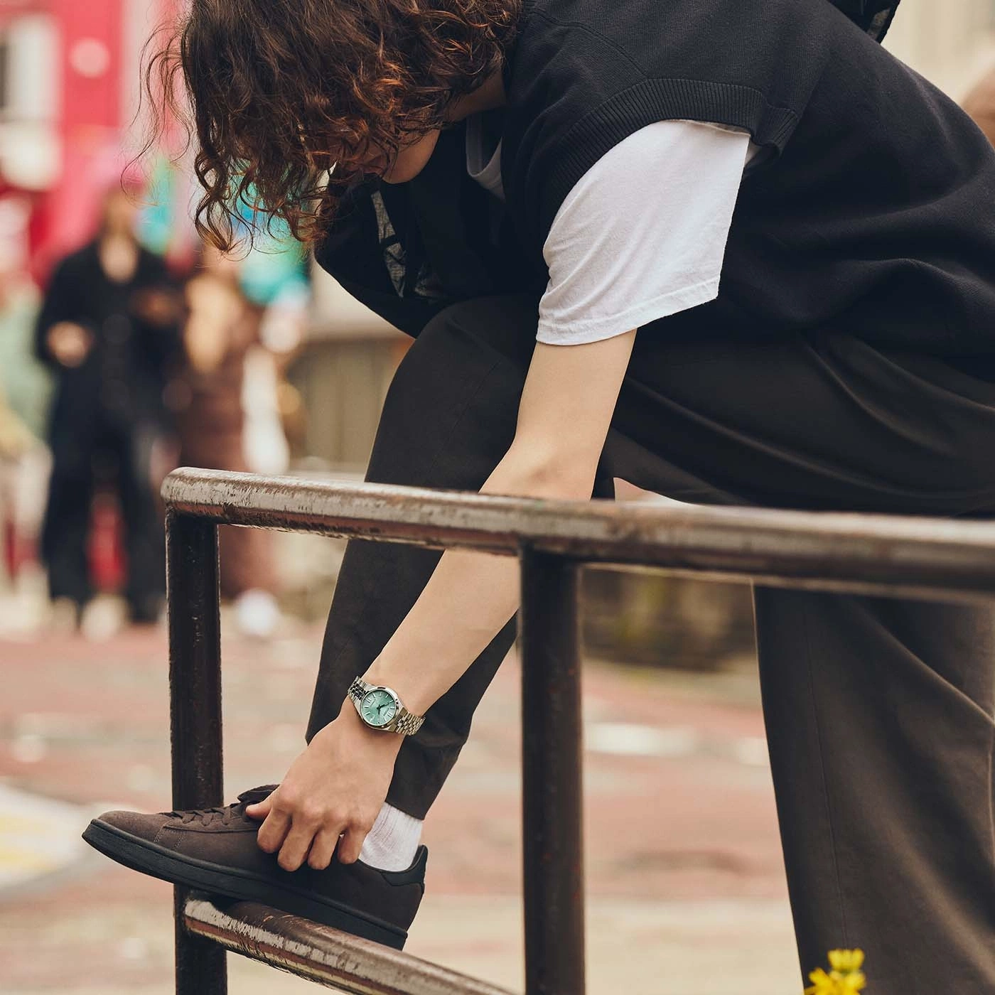 Person tying shoe, wearing watch and dark pants