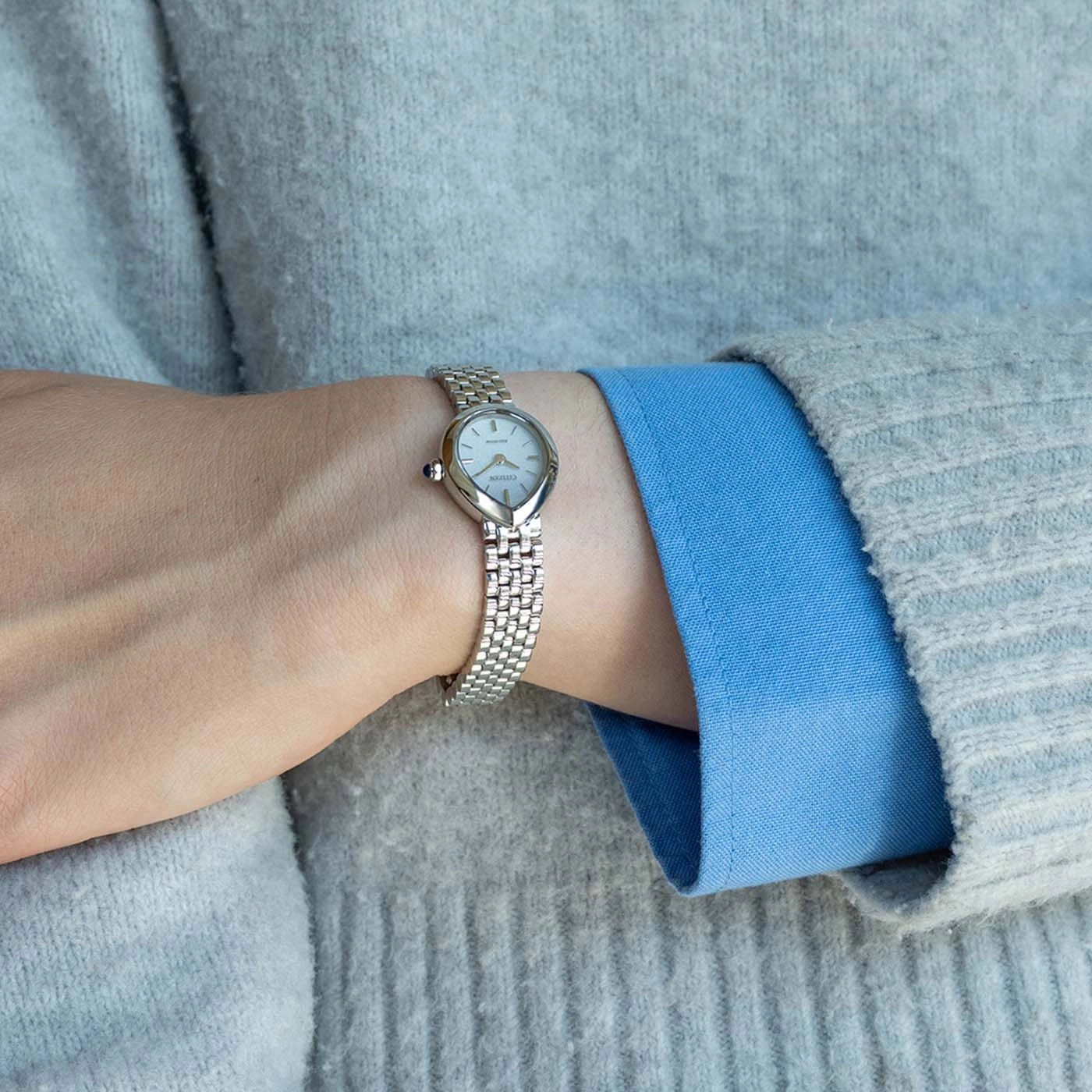 A woman's wrist with a silver watch and grey sweater.