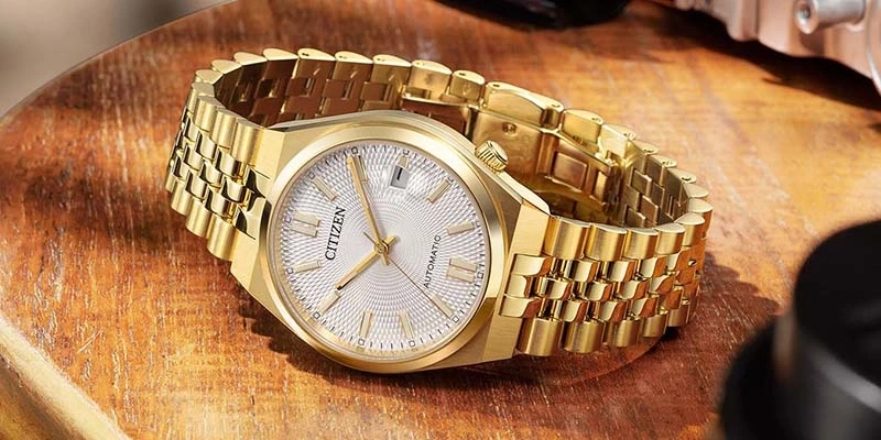 A gold Citizen automatic watch with a textured dial on a wooden surface.