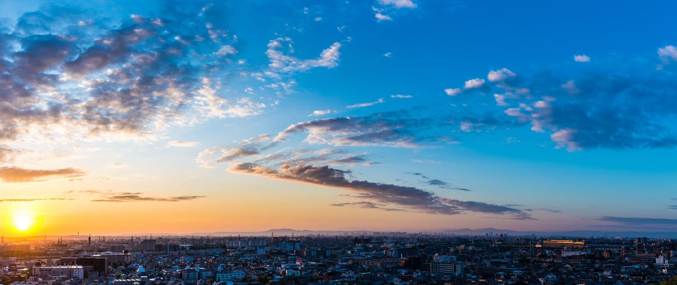 Cityscape at sunset with a vibrant sky and scattered clouds over buildings.