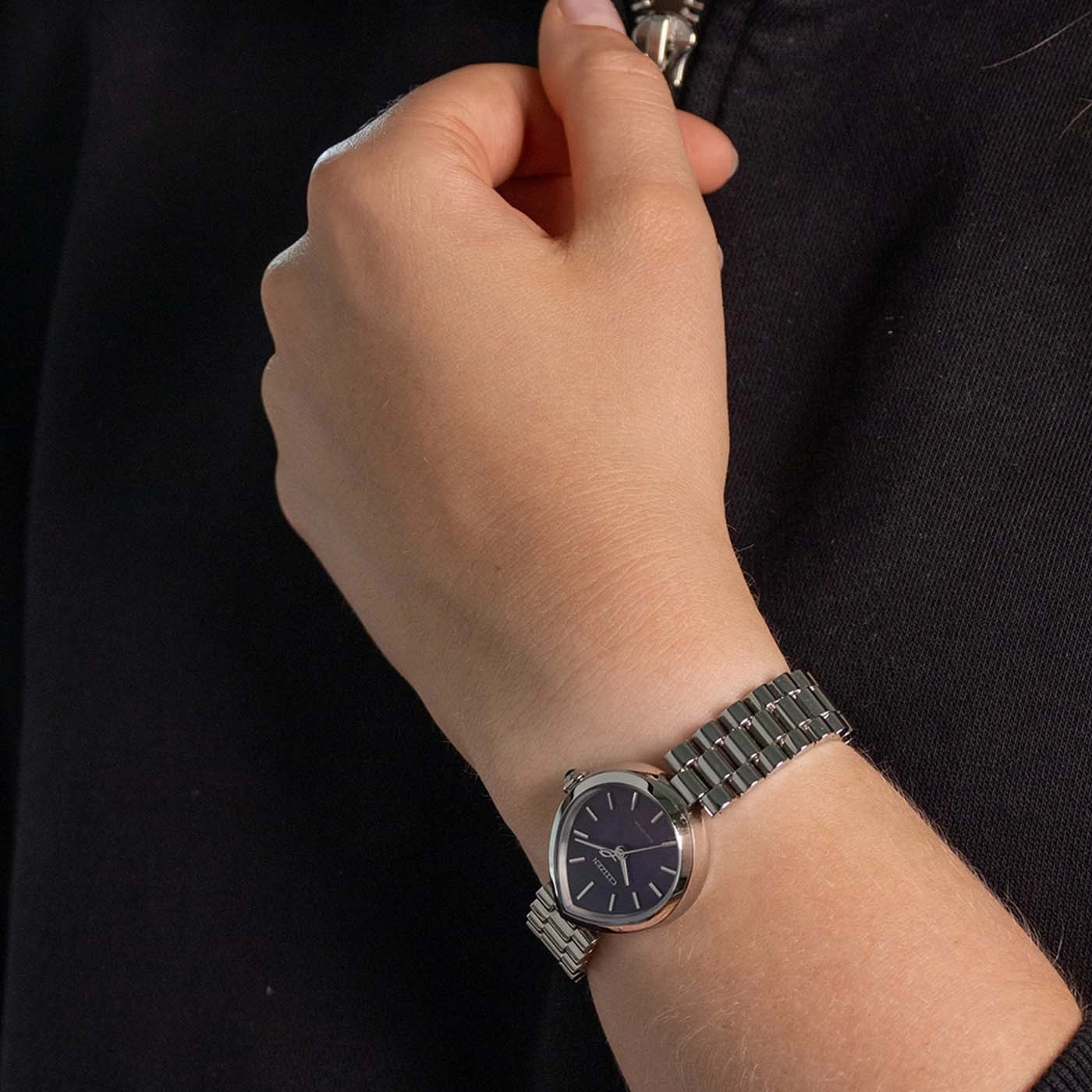 A woman's hand wearing a silver watch with a dark face.