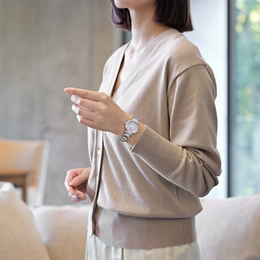 Woman wearing a beige cardigan and a silver watch, pointing.