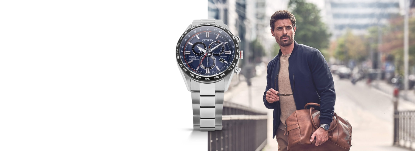 Man wearing a Citizen watch, holding glasses and a bag, walking on a street.