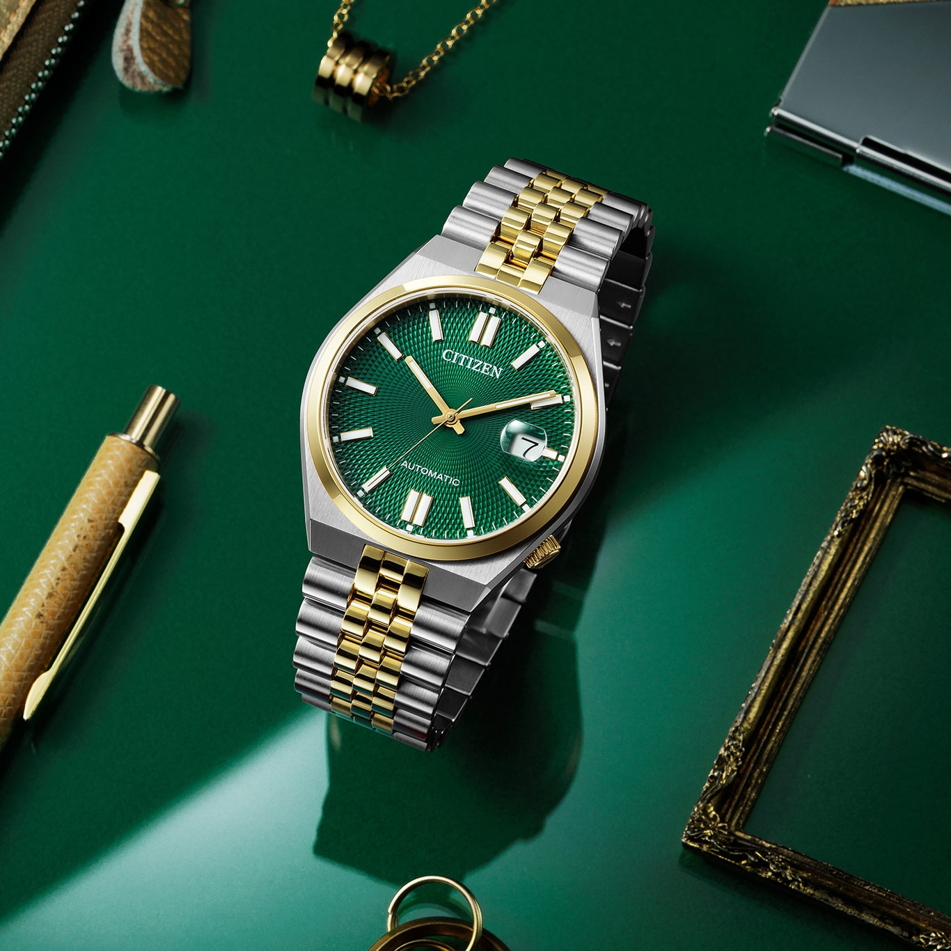 Citizen watch with green face and gold accents on a green surface.