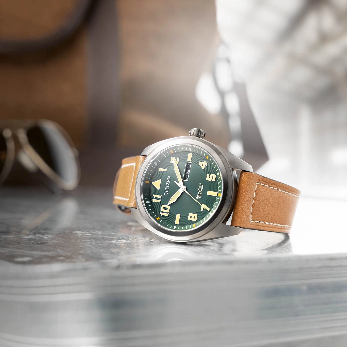 Citizen watch with green face and brown leather strap on a reflective surface.