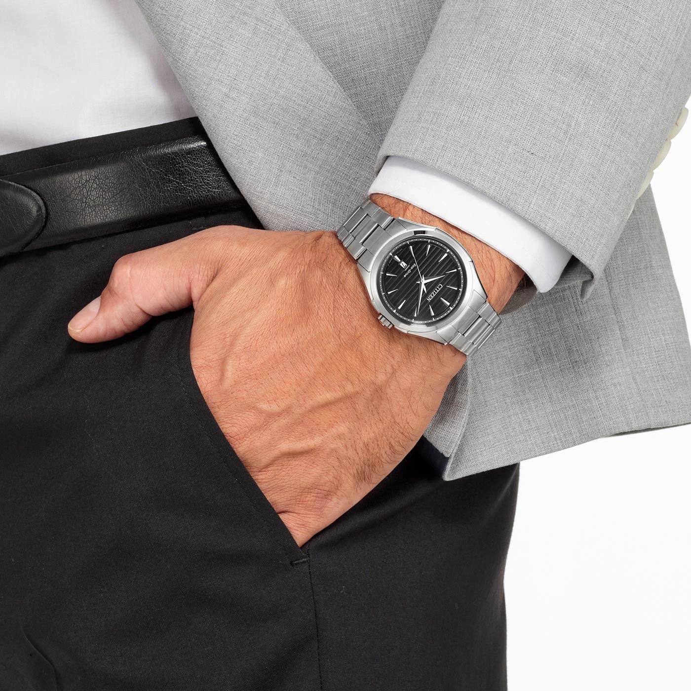 Man wearing a watch, suit, and black pants with his hand in his pocket.