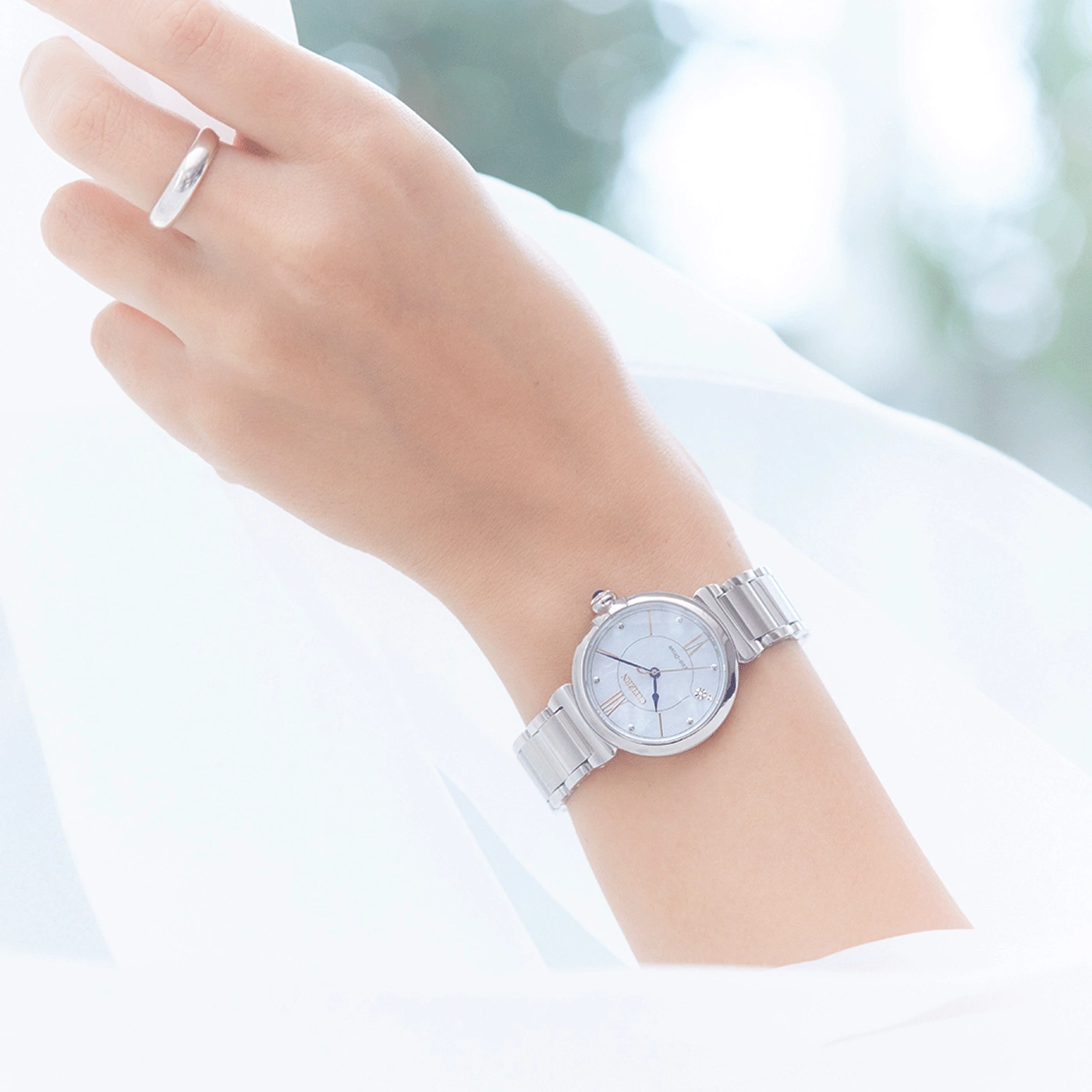 Wrist with a silver watch and a ring, white background, elegant