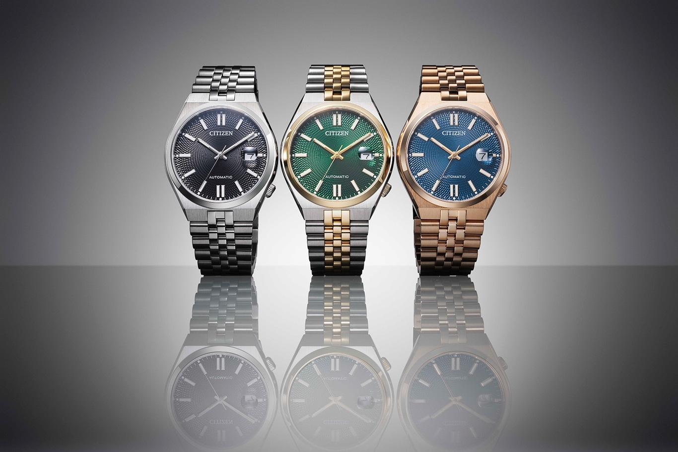 Three Citizen watches with different colored faces and bands, reflected.