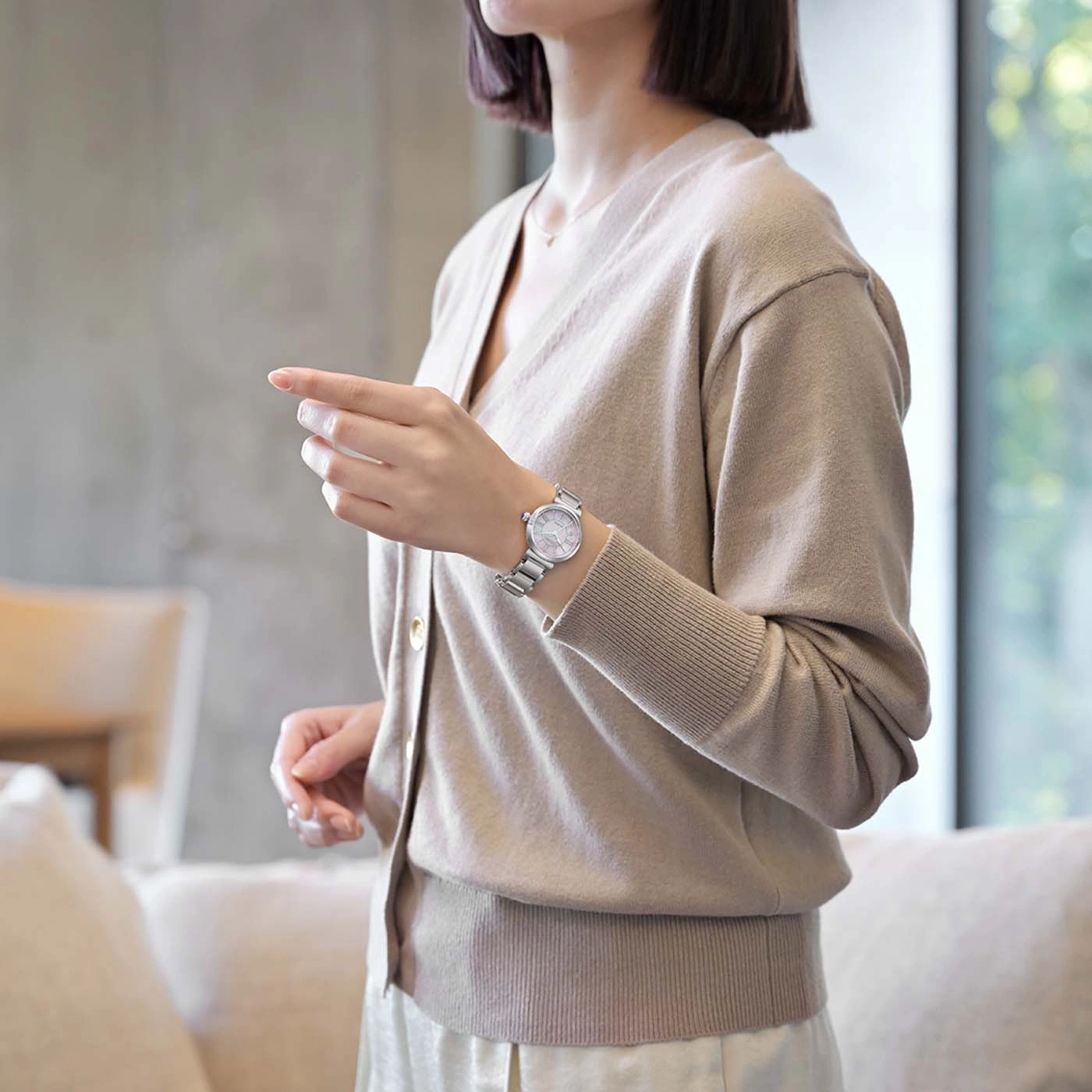 Woman wearing a beige cardigan and a silver watch, pointing.
