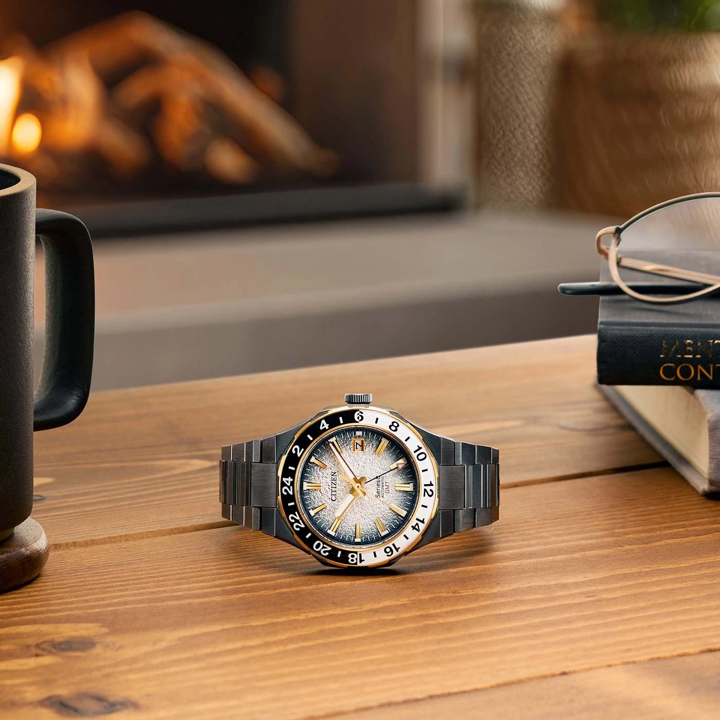 Watch on a wooden table with a mug, glasses, and a book.