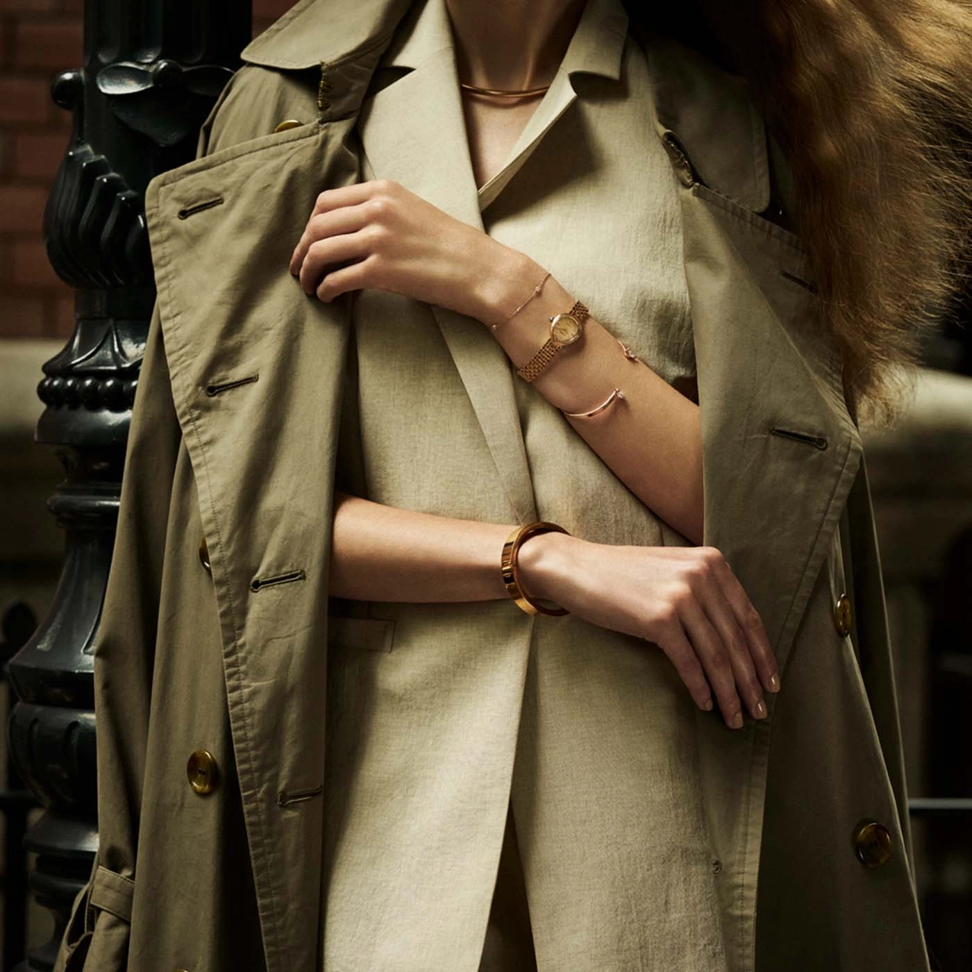 Woman wearing a trench coat and jewelry, close-up of arms.