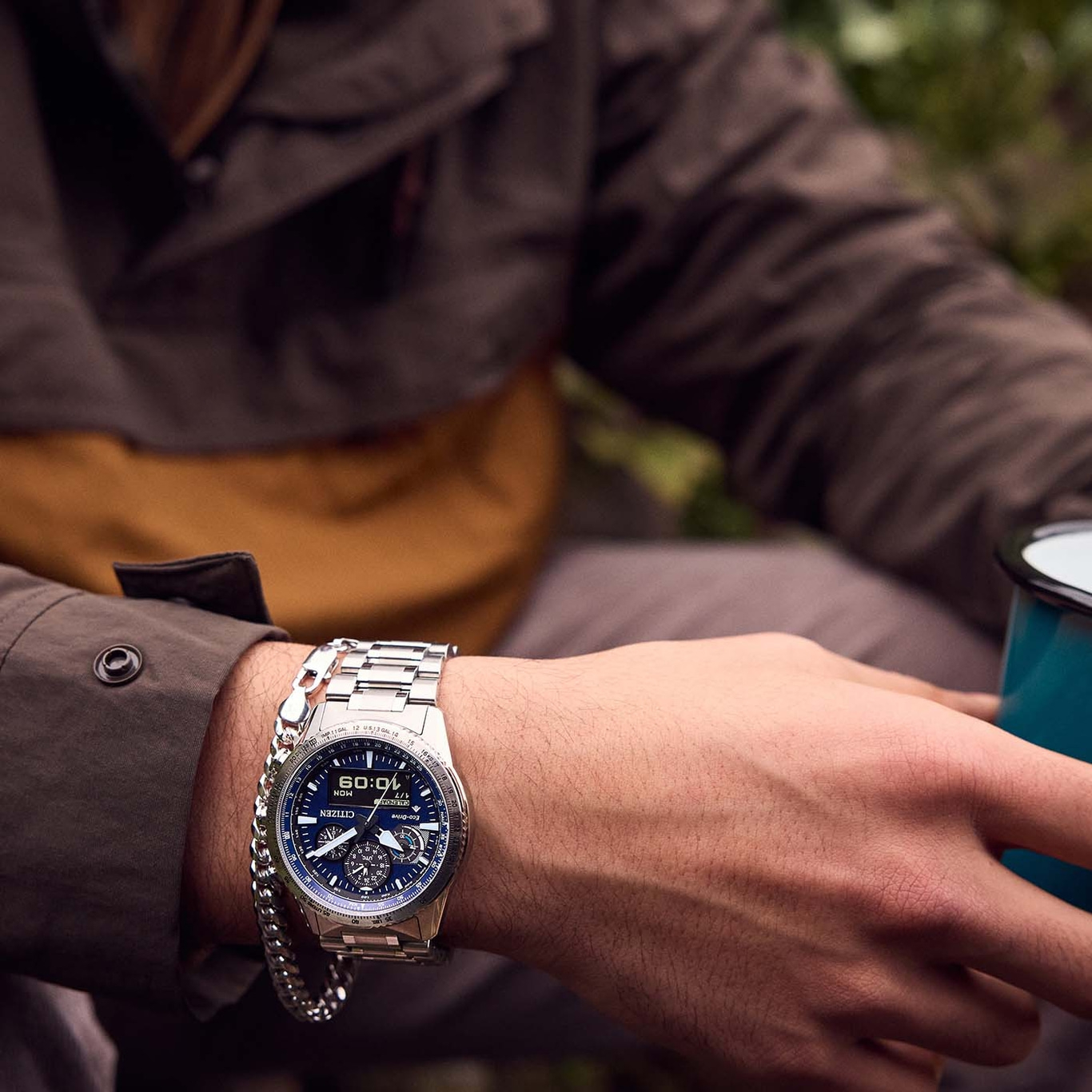 Man wearing a Citizen watch and a bracelet, holding a mug.