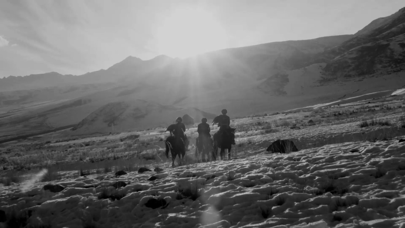 Horses and riders in a snowy mountain landscape, black and white photography.