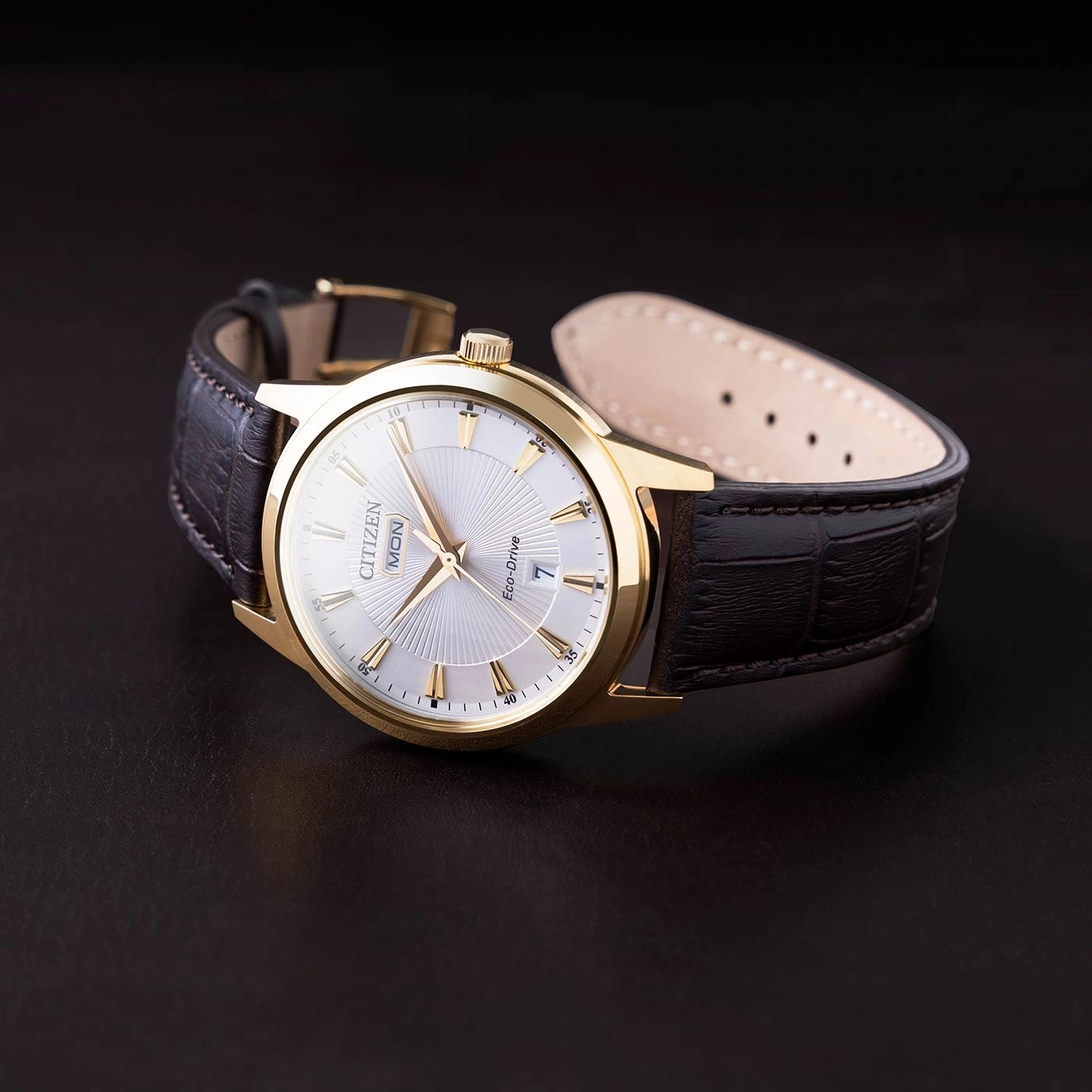Gold Citizen watch with a leather strap on a dark surface.
