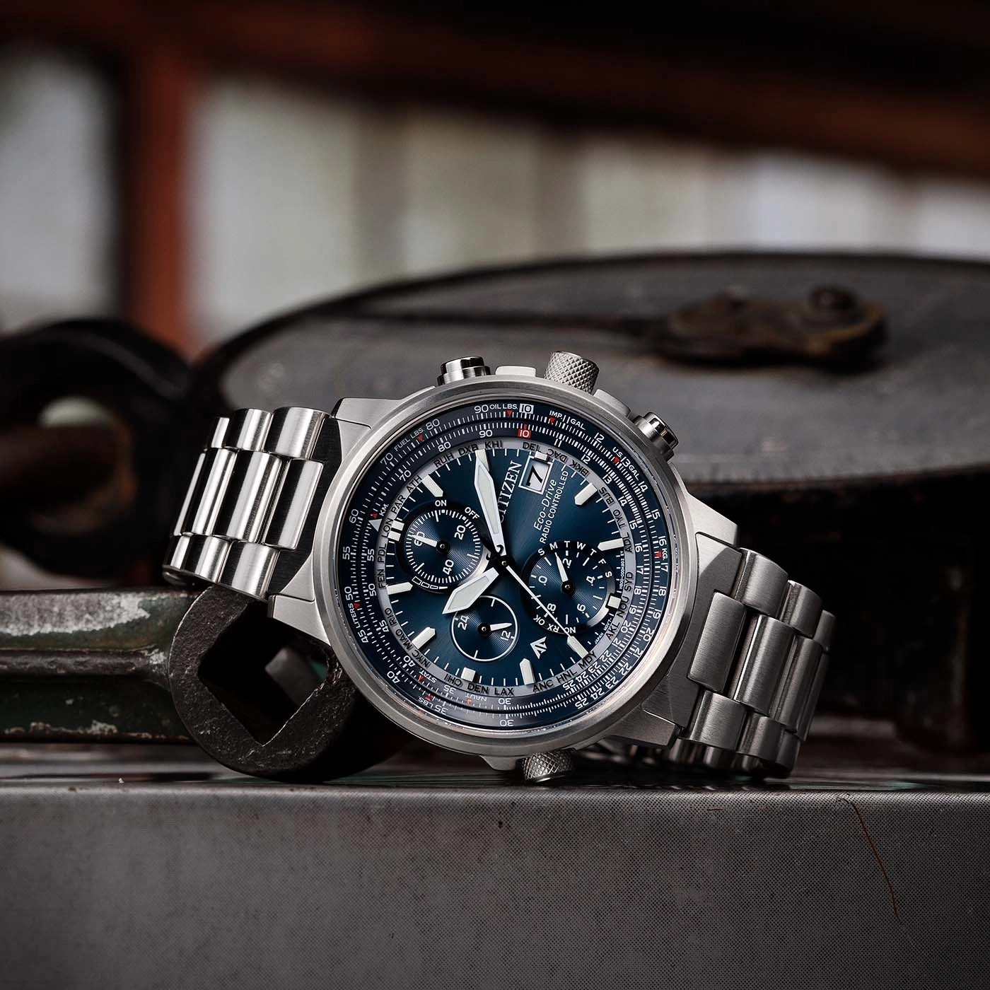 Citizen watch with blue face and metal band on a metallic surface.