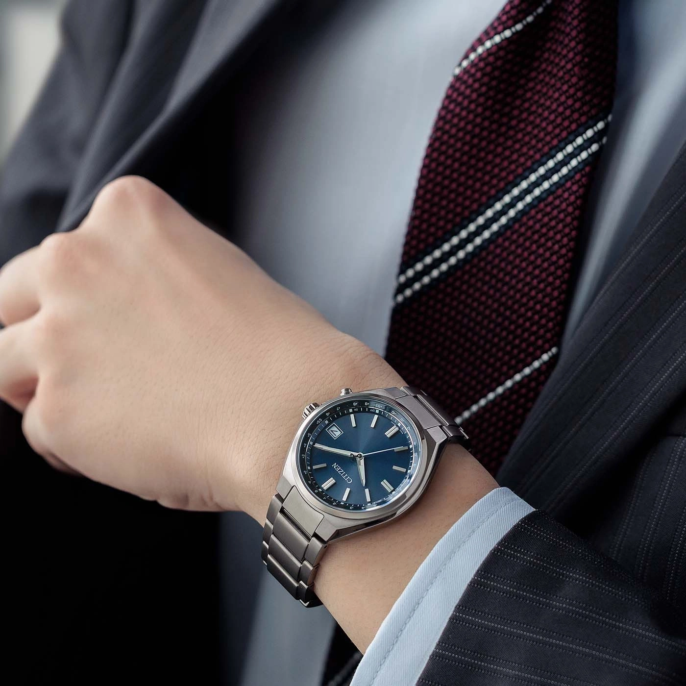 A man in a suit wears a blue Citizen watch on his wrist.