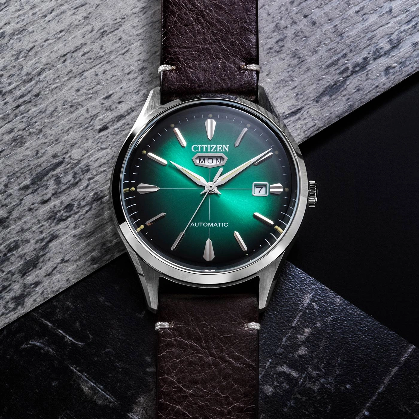 Citizen watch with green dial and brown leather strap on a textured surface.