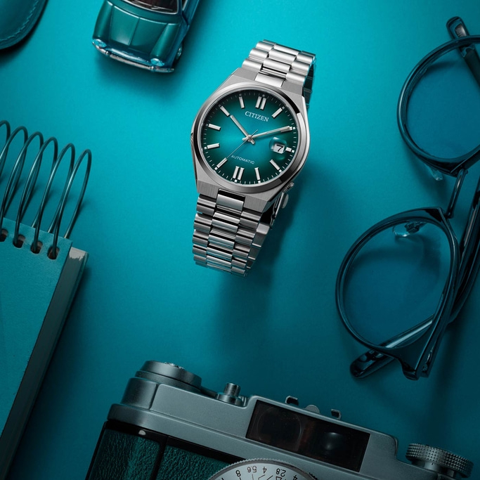 Citizen watch, glasses, camera, toy car, and notebook on a blue surface.