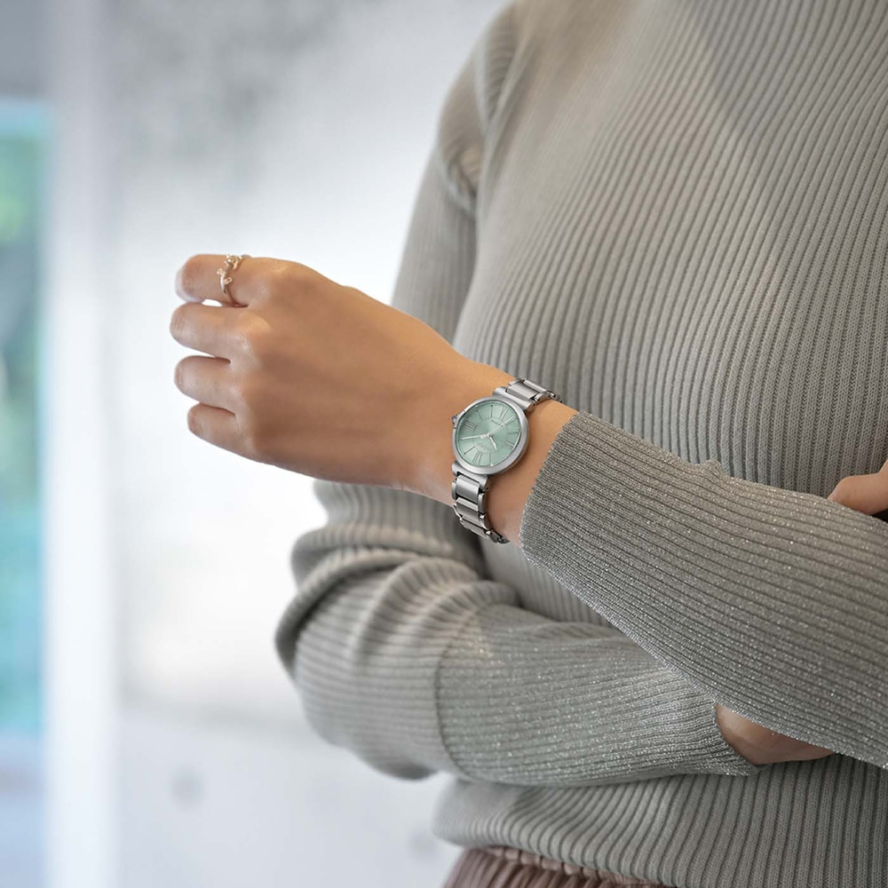 A woman wearing a silver watch and a grey sweater.