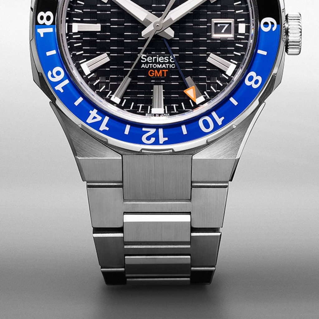 Close-up of a silver watch with a blue bezel and black dial.