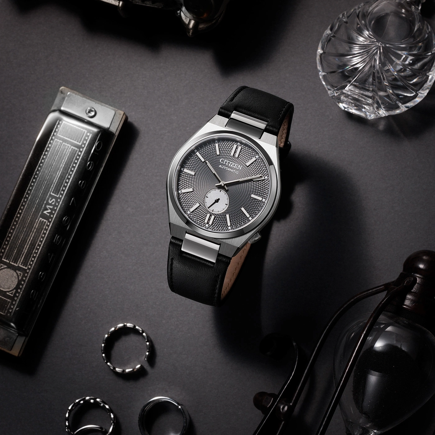 Citizen watch with black leather strap and accessories on a dark surface.