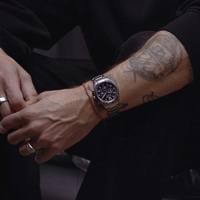 Close-up of a man's tattooed arm wearing a watch and rings.