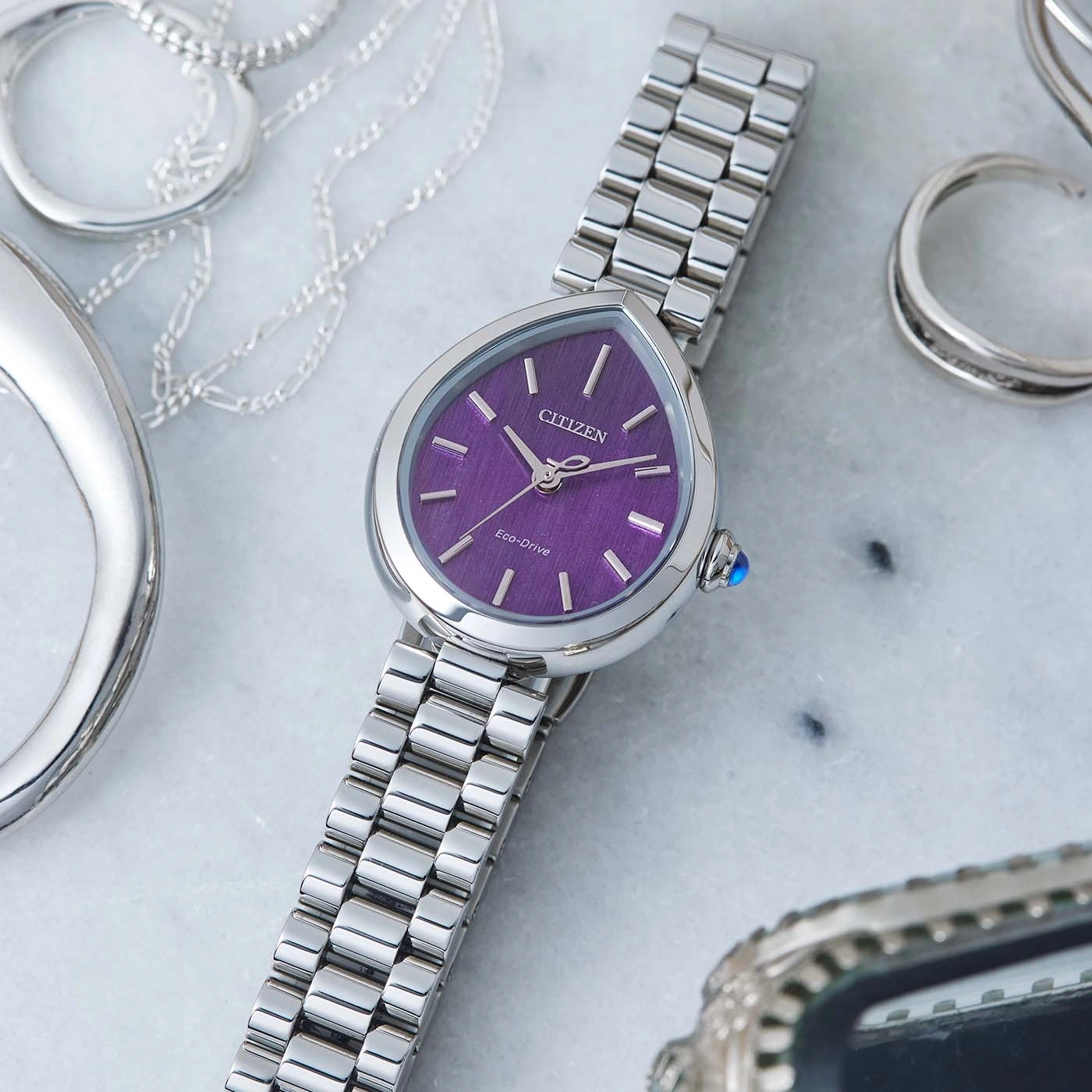 Silver watch with purple face and silver bracelet, surrounded by jewelry.