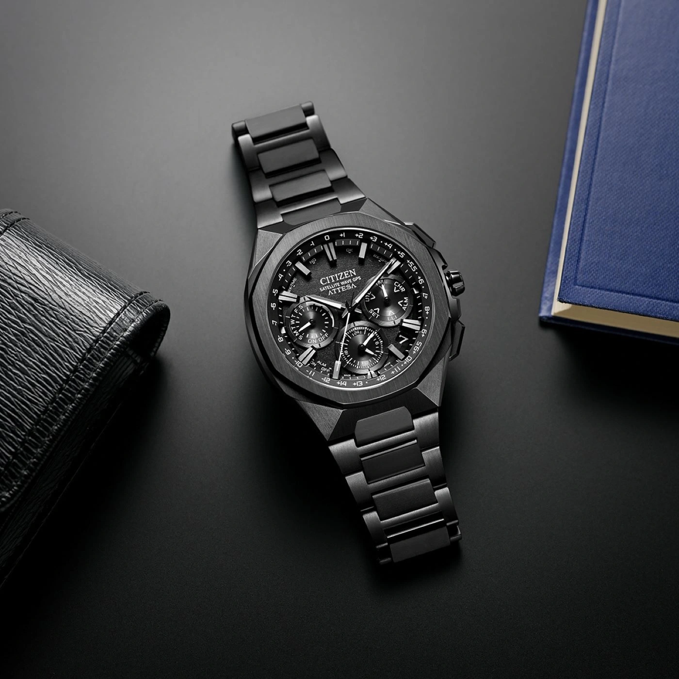 Black Citizen watch on a black surface with a wallet and a book.
